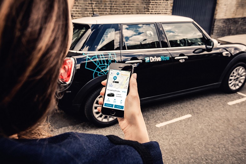 Young woman booking a DriveNow shared car using her smartphone drivenow-brussels