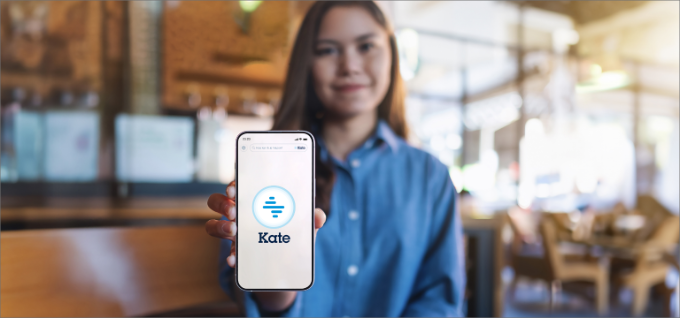 Vrouw toont het scherm van haar smartphone. Op het scherm zie je het logo van Kate. 